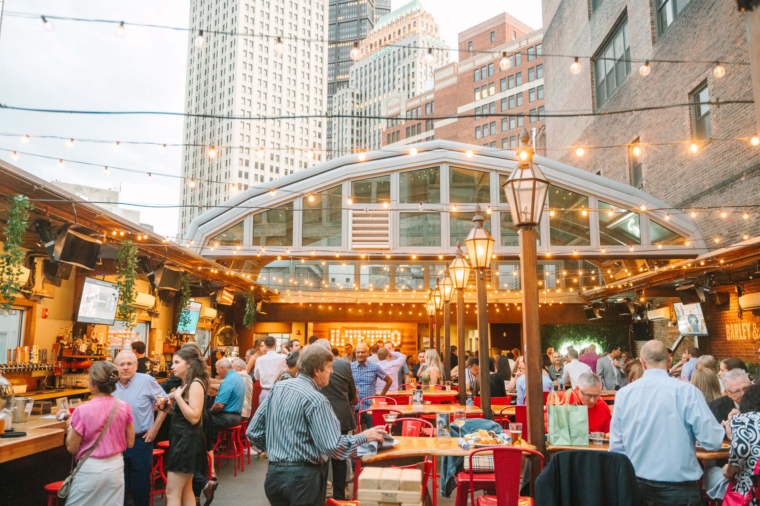 Wide angle view of rehearsal dinner after-party, string lights illuminating outdoor patio as guests mingle