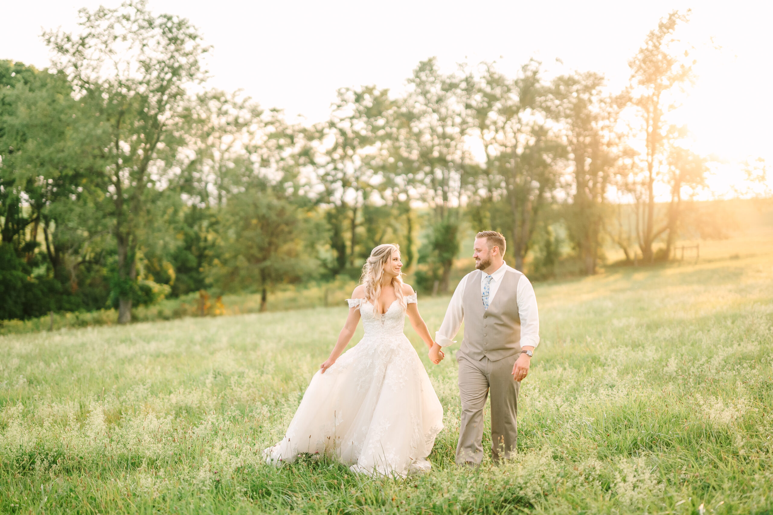 A romantic portrait of newlyweds walking hand in hand through golden light, creating long shadows across a natural landscape