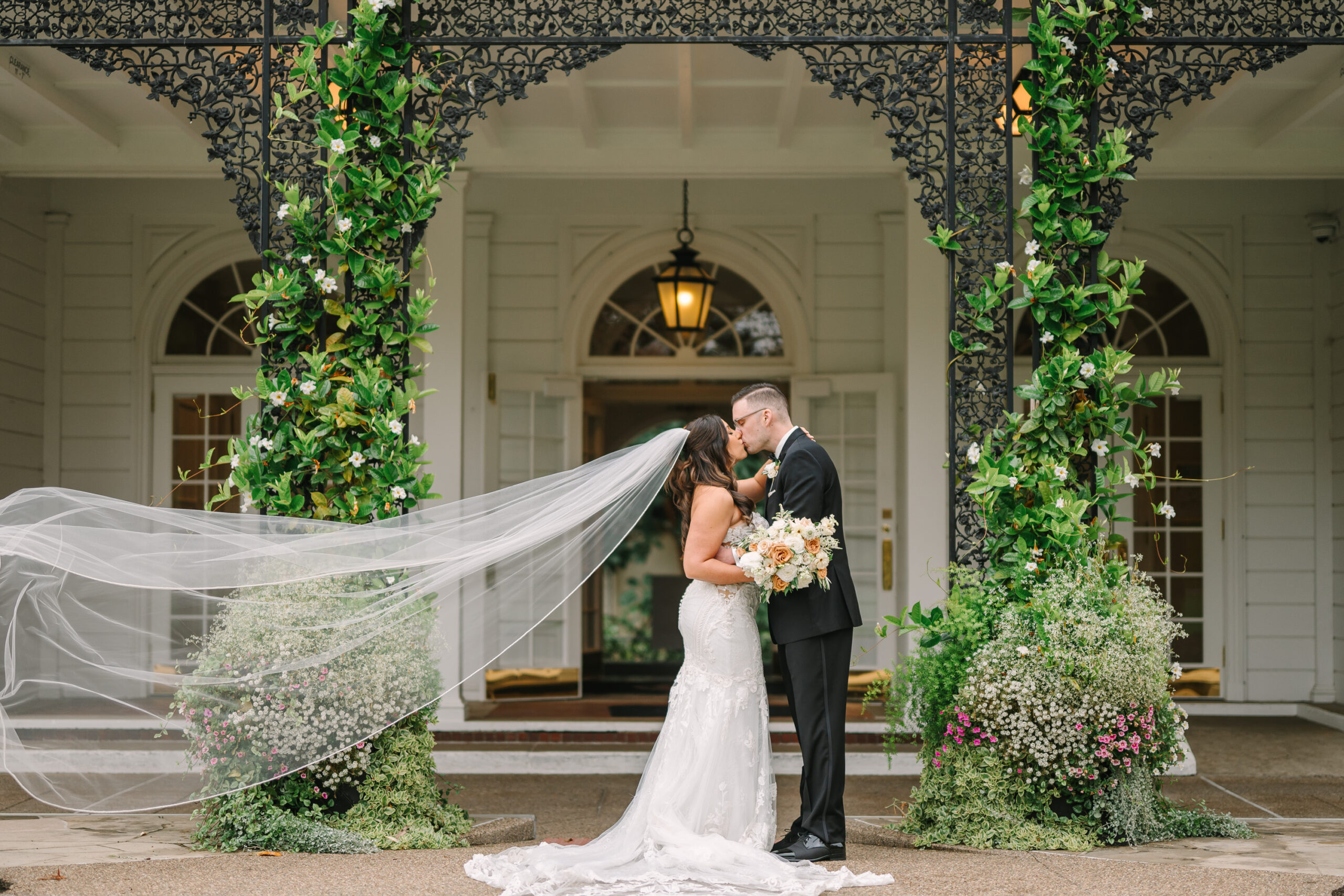 A couple kisses under the entryway of Fox Chapel Golf Club as the bride's veil blows int he wind