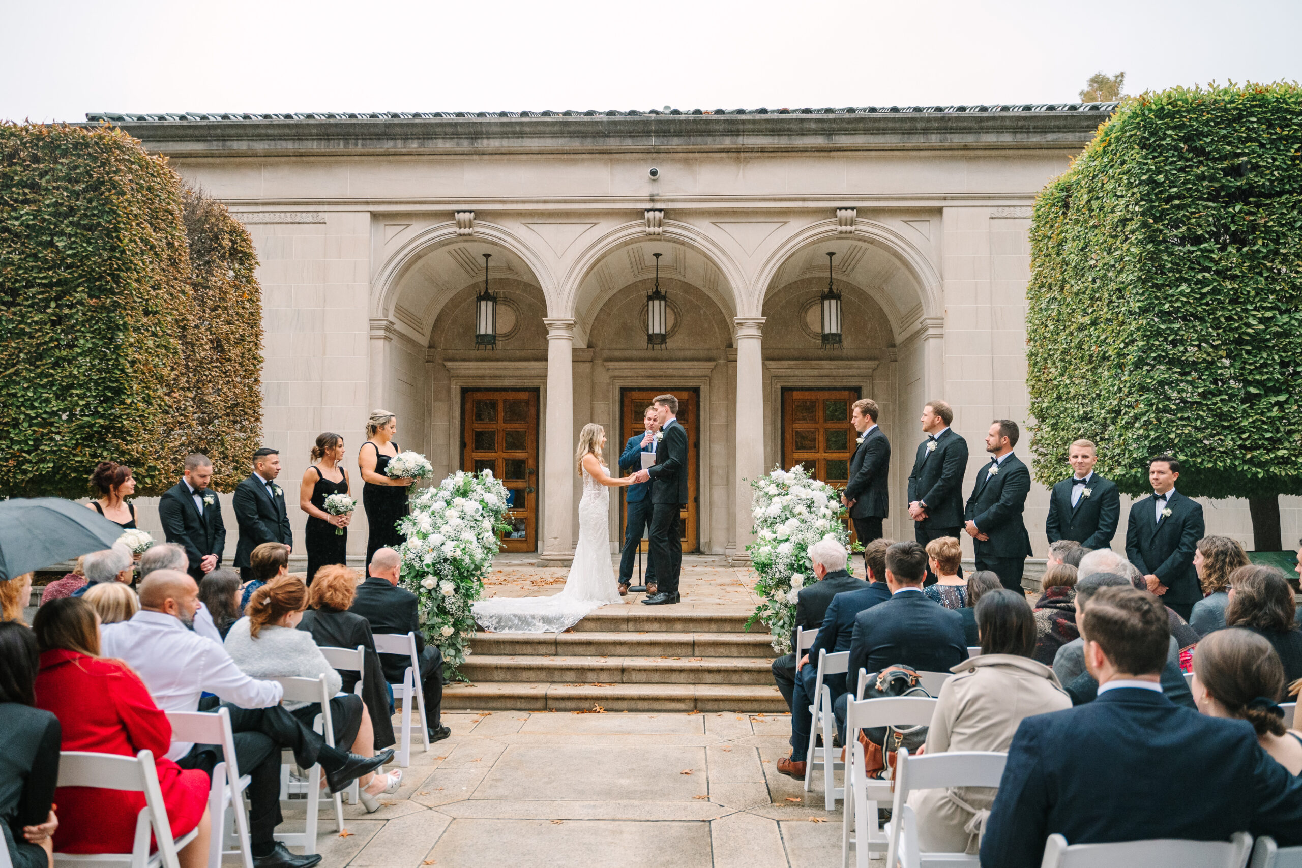 A couple joins hands during their ceremony on the steps of the Frick Museum.